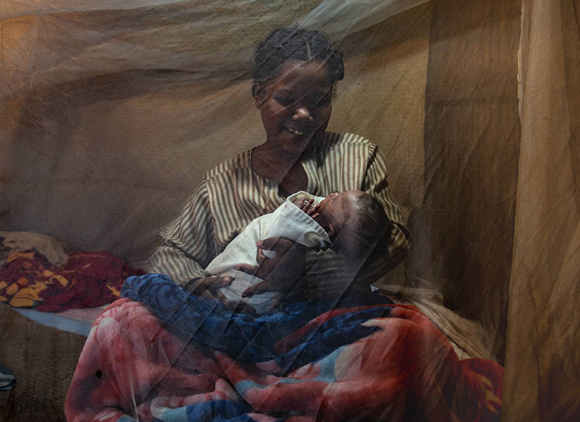 A smiling mother cradles her newborn beneath a mosquito net in Madagascar.