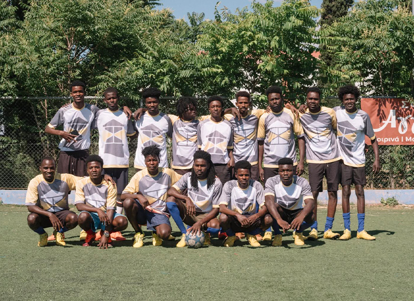A young football team in matching jerseys poses on a pitch, one row standing and one kneeling, with a ball at their feet.