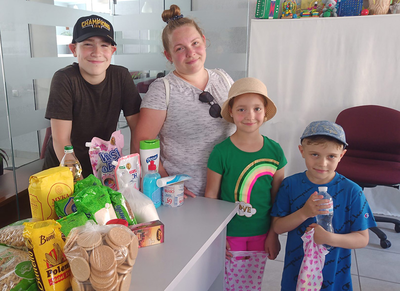 A mother and three children smile behind a table of donated food and household supplies.