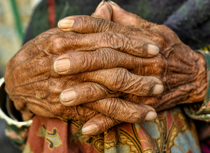 Close-up of an elderly person's weathered hands clasped together.