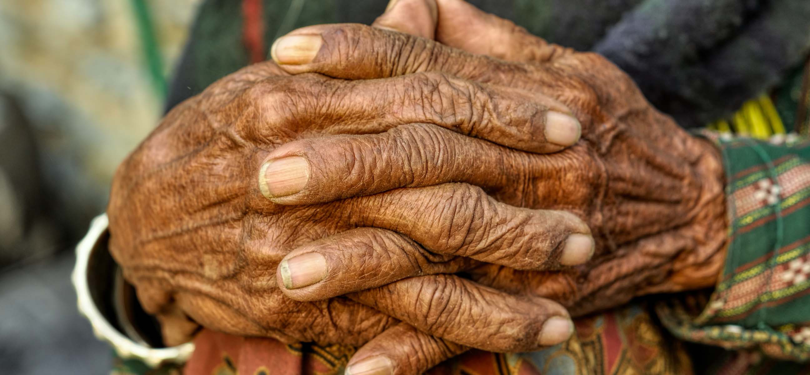 Close-up of an elderly person's weathered hands clasped together.