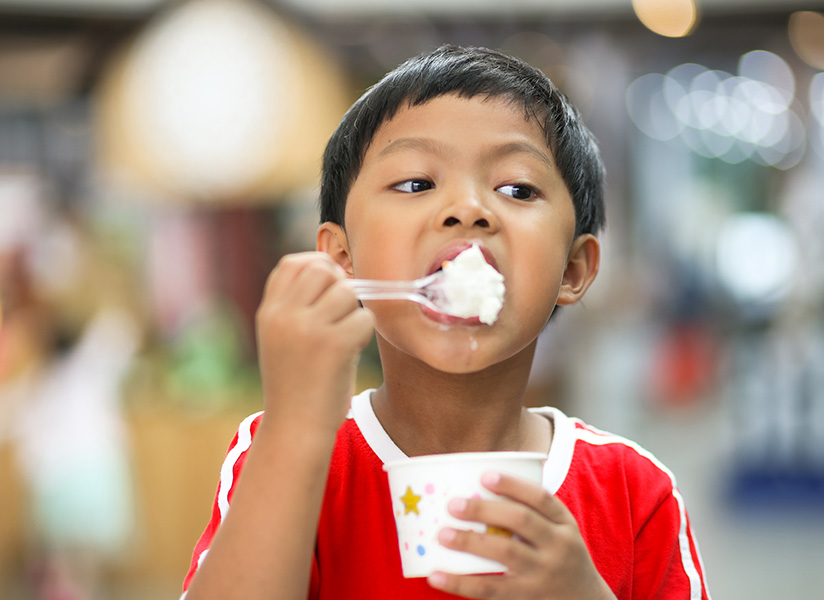 A young boy in a red shirt eats a spoonful of rice from a paper cup.