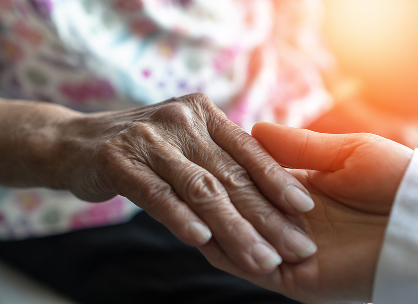 A caregiver's hand gently holds an elderly person's hand.