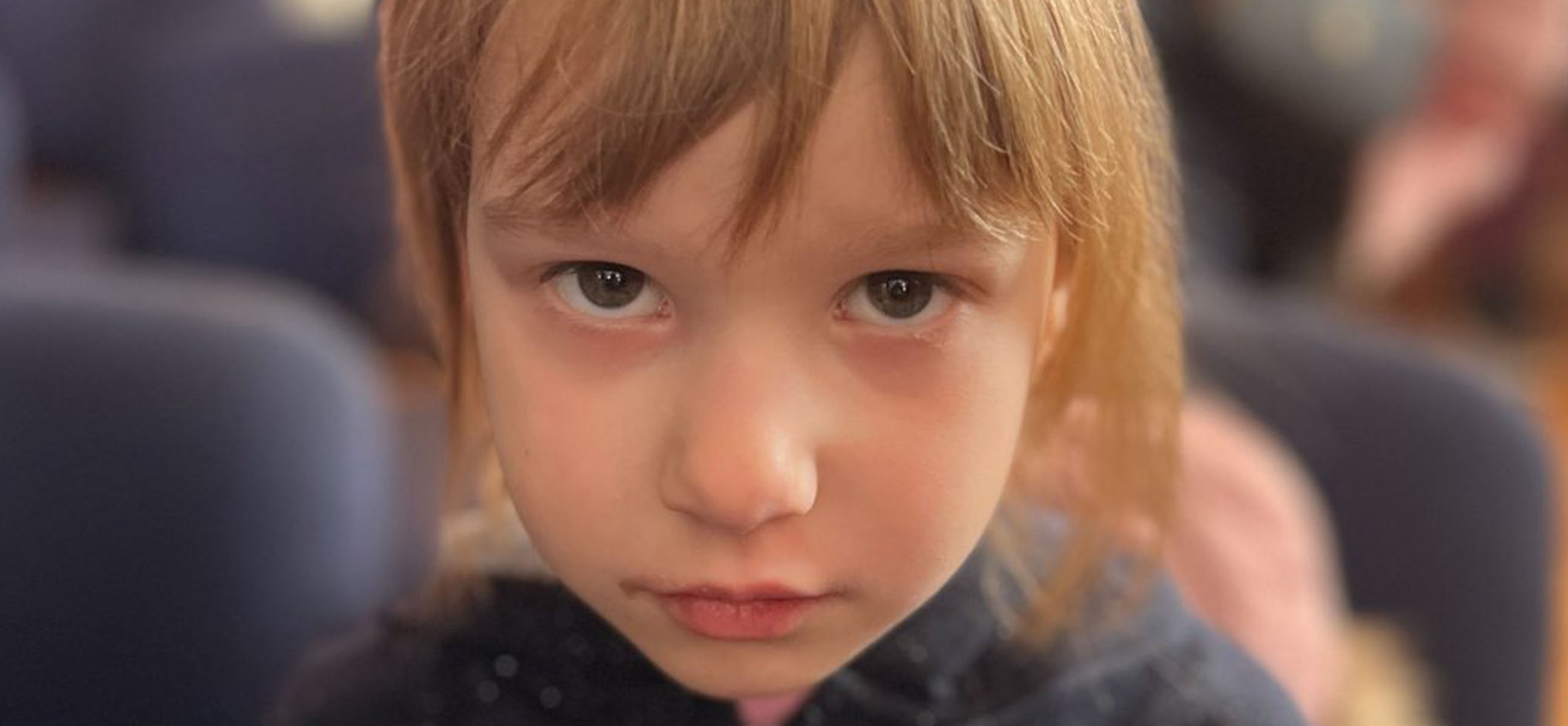 A young girl with a serious expression looks directly at the camera.
