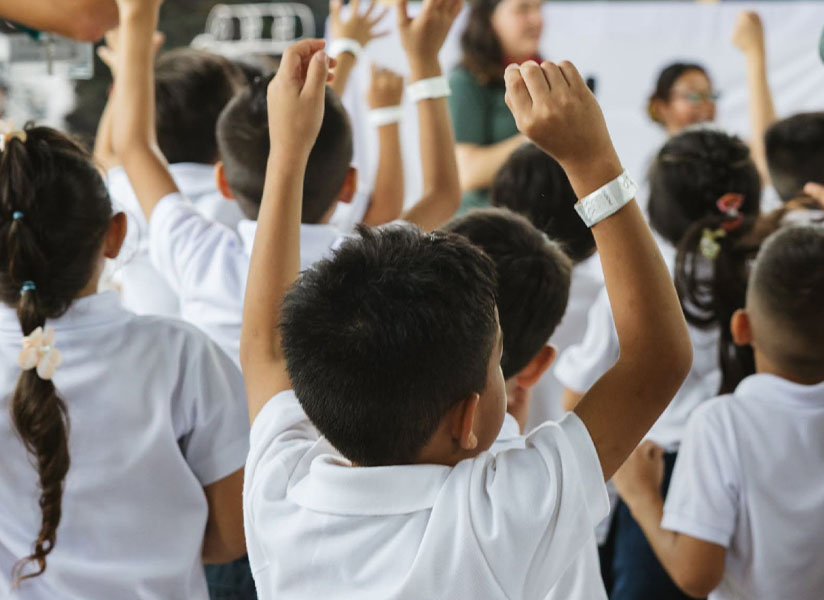 A room full of children eagerly raise their hands at a camp gathering.