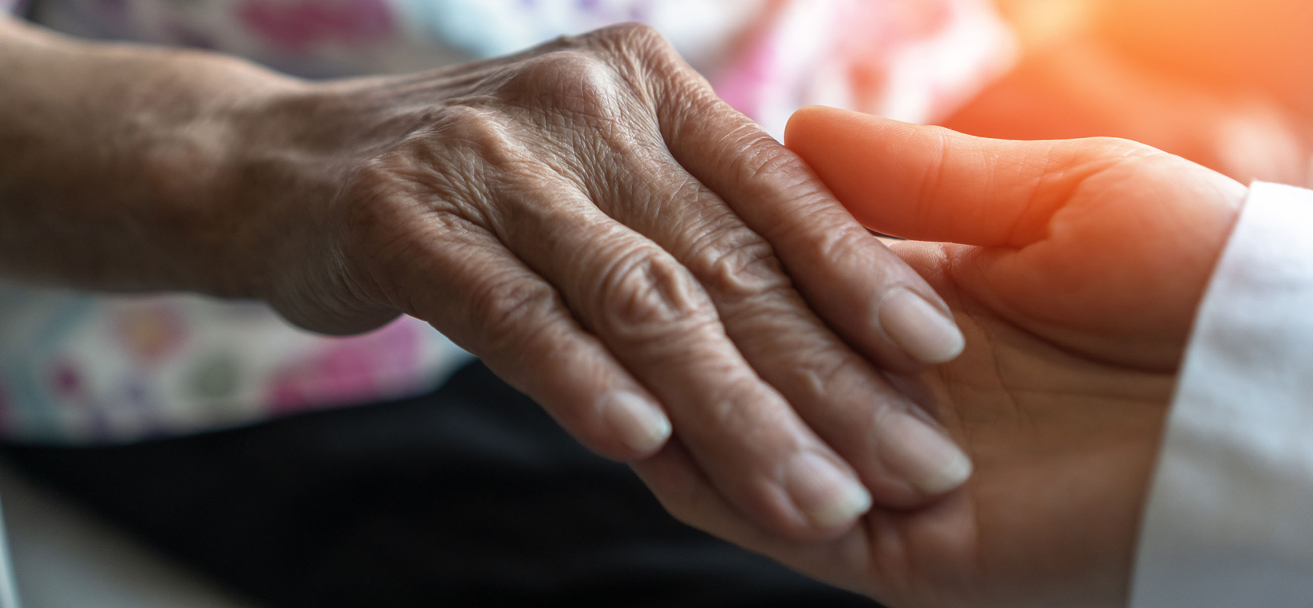 A caregiver's hand gently holds an elderly person's hand.