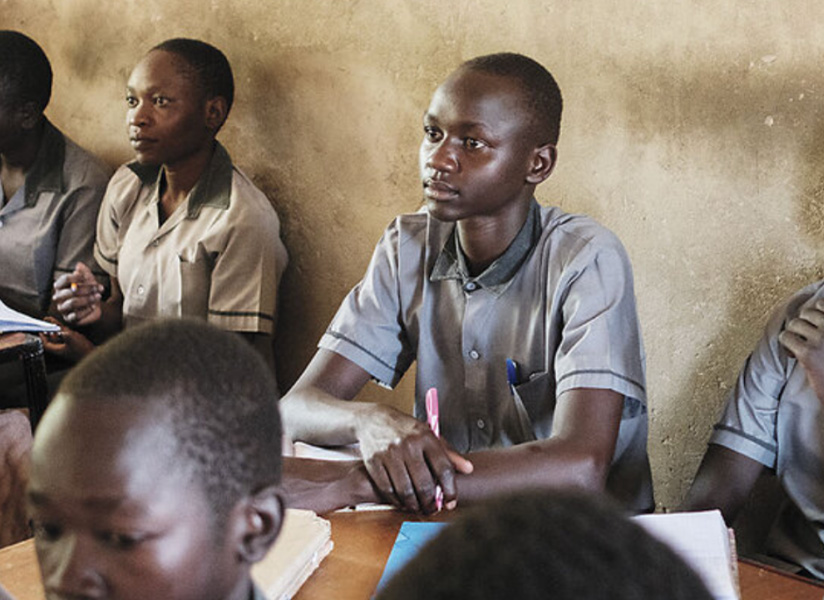 Students in gray school uniforms listen attentively from their desks in a classroom.