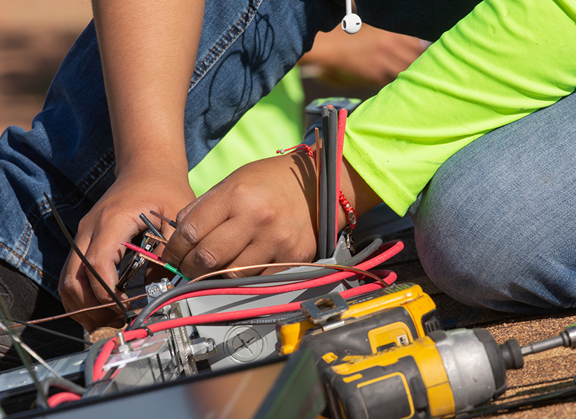 Close-up of hands connecting colored electrical wires, with a power drill nearby.