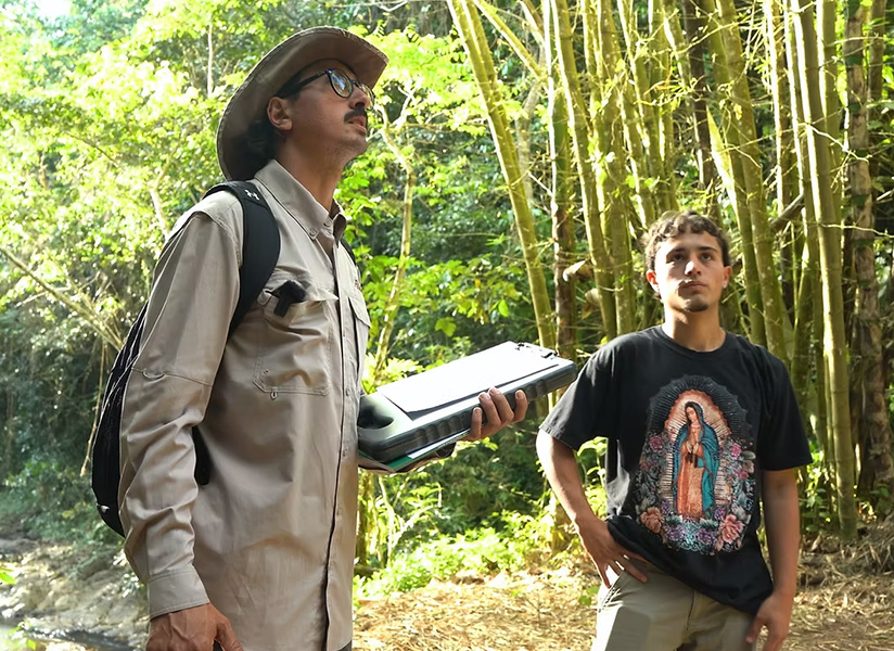 An Asekia staff member in a wide-brimmed hat stands with a young man in a bamboo forest.