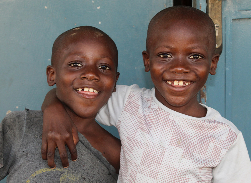Two grinning young boys pose cheek to cheek in front of a blue wall.