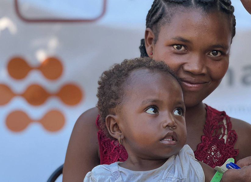 A smiling mother holds her toddler during a nutrition health screening.