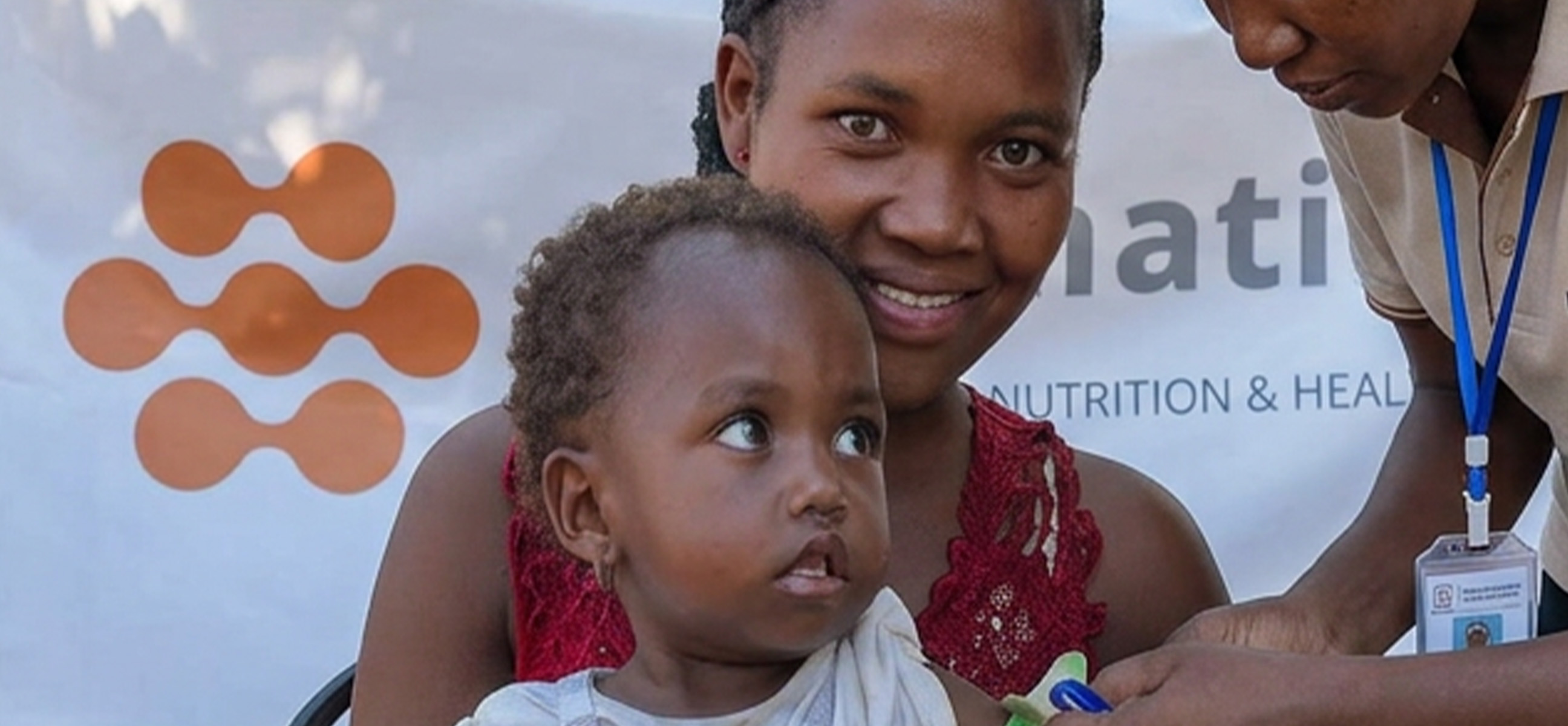 A smiling mother holds her toddler during a nutrition health screening.