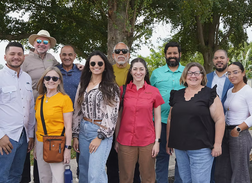 A group of Asekia staff and partners pose together outdoors beneath trees.