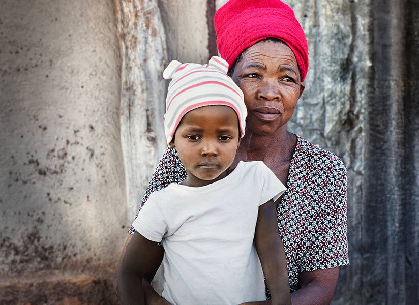 An older woman in a red headwrap holds a young child in a striped knit cap.