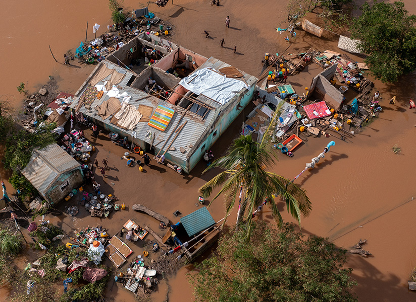 An aerial view of a damaged house surrounded by brown floodwater, with belongings spread out to dry.