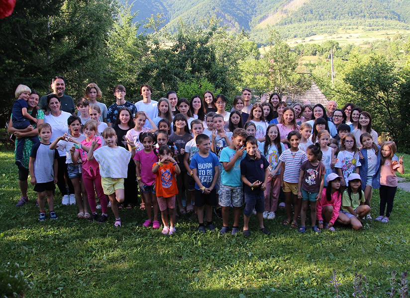 A large group of children and adults pose together on a grassy lawn in front of trees.