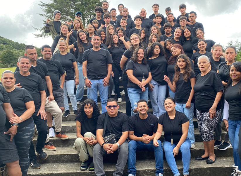 A large team in matching black shirts poses on outdoor steps.