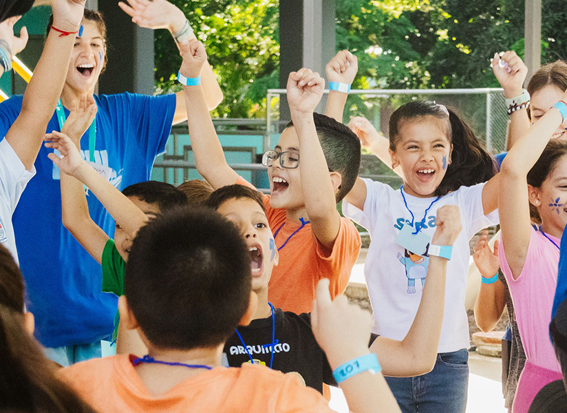 Excited campers with painted faces raise their fists and cheer together outdoors.