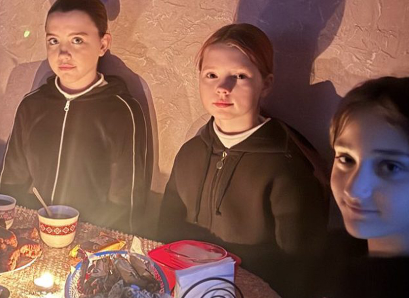 Teenage girls gather around a candlelit table with warm drinks and snacks.