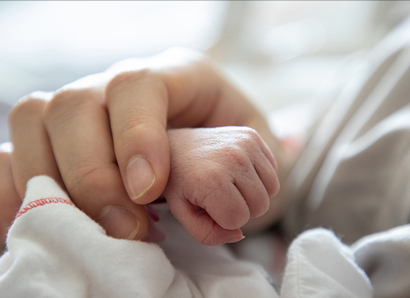 Close-up of a newborn's tiny fist wrapped around an adult's finger.