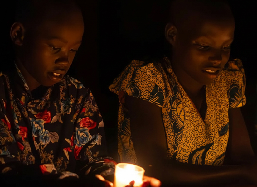 Three young people sit in the dark, their faces lit by small candles.