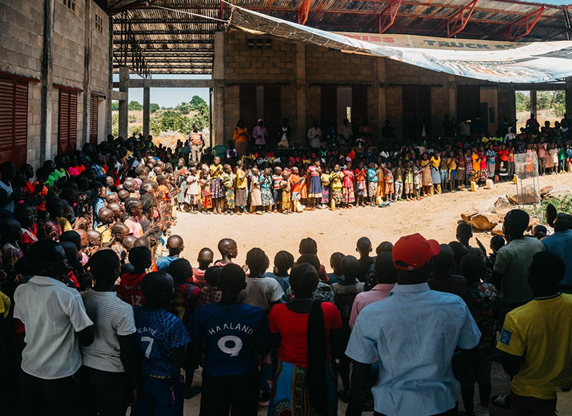 A large crowd gathers in a wide circle around an open courtyard, watching a community event.
