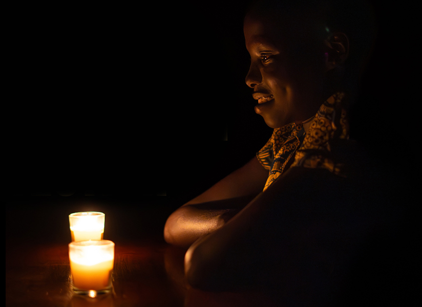 A smiling young woman sits in the dark beside a glowing candle.