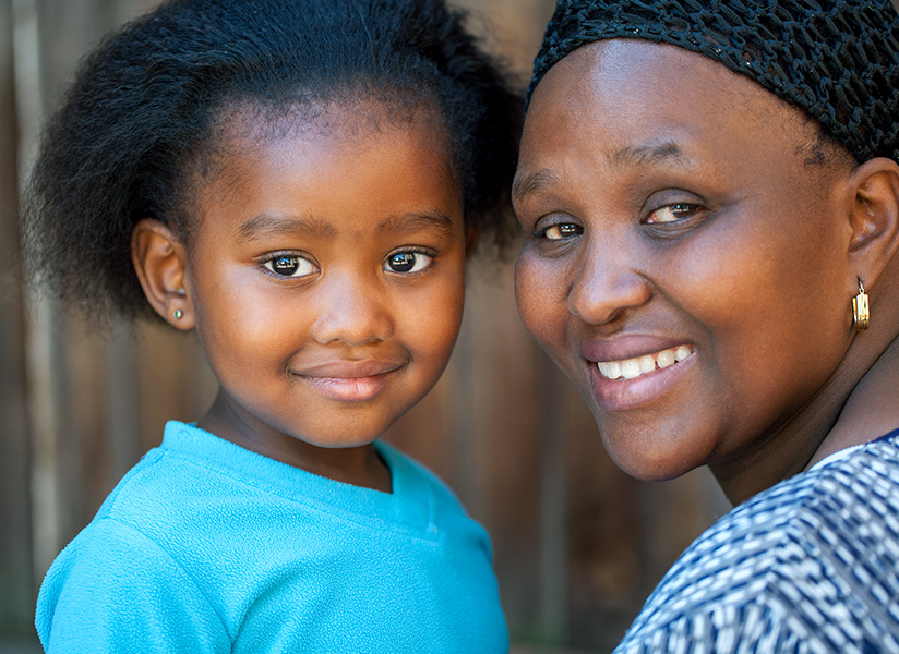 A smiling young girl in a blue shirt poses cheek to cheek with a smiling woman.