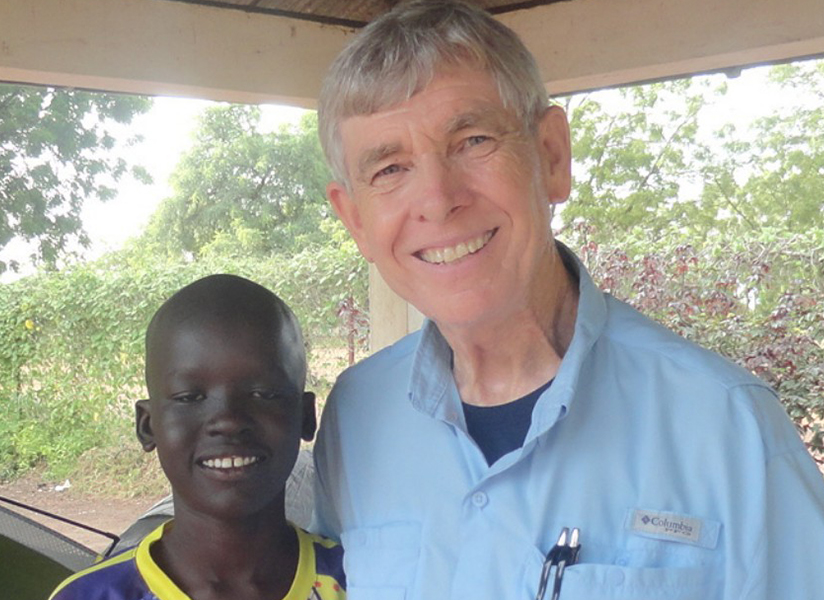 A smiling boy stands beside a smiling older man in a light blue shirt.