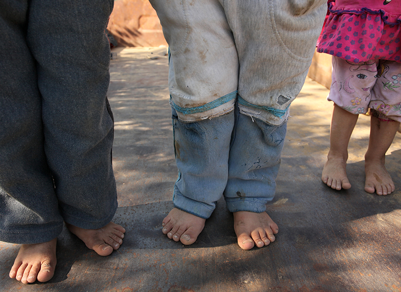 Close-up of several children's bare feet standing on a dusty sunlit floor.