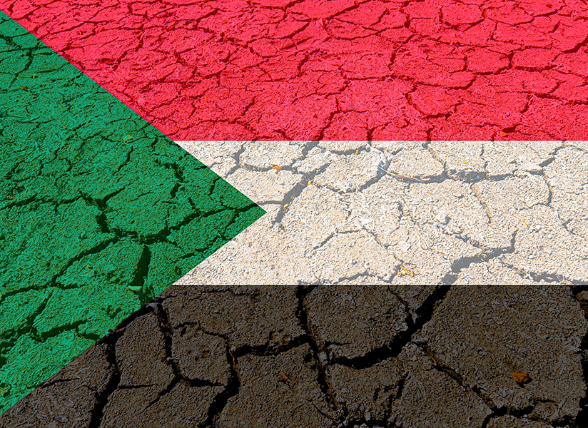 The flag of Sudan printed over dry, cracked earth.