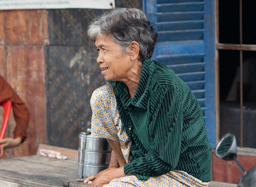 An older woman in a green striped shirt sits outdoors looking into the distance.