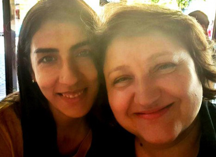 Two smiling women pose cheek to cheek outdoors.