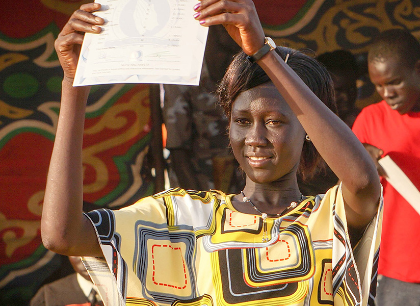 A smiling young woman in a colorful dress holds up a certificate.
