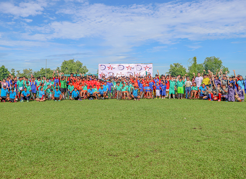 A huge crowd of children and coaches in colorful jerseys pose together on a football field.