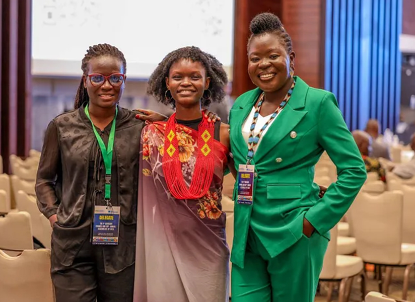Three smiling women with conference badges pose together at an event.