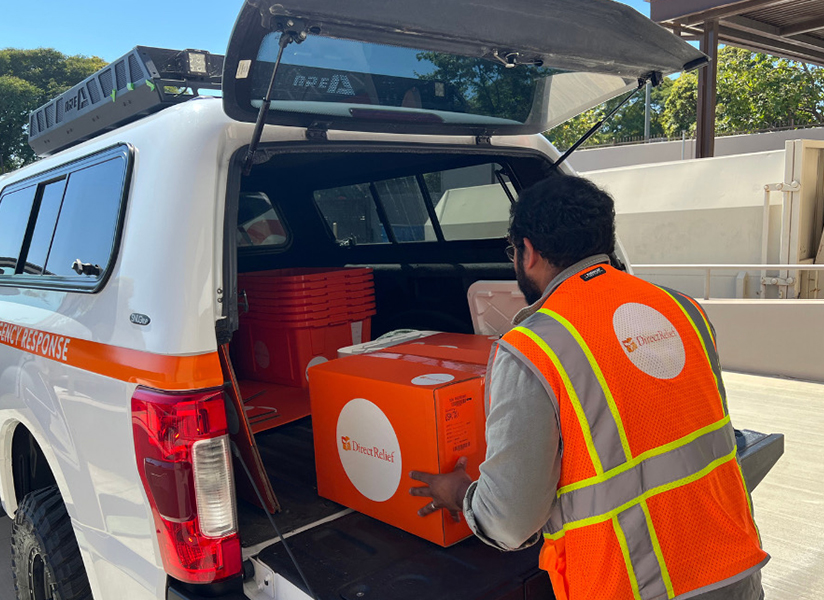 A worker in an orange safety vest loads Direct Relief boxes into the back of a white truck.