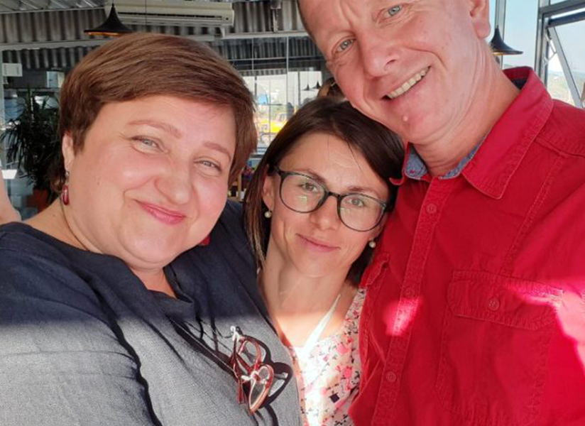 Three smiling adults pose close together for a selfie.