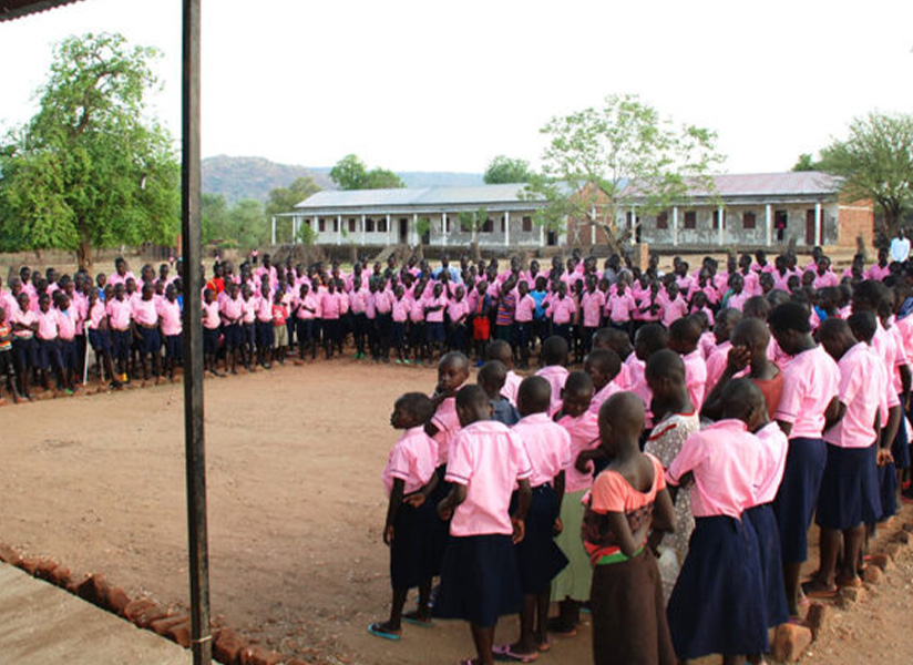 Rows of students in pink school uniforms stand in formation in a schoolyard.