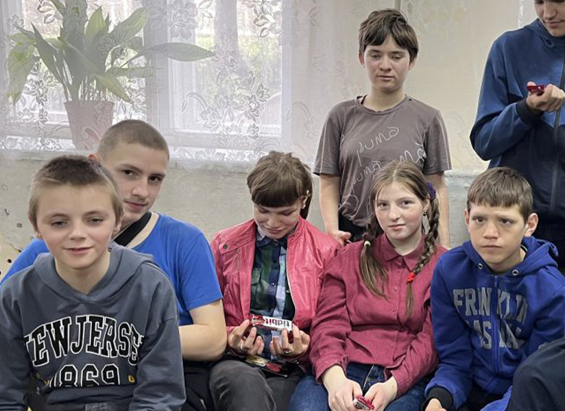 A group of children and teenagers gather together indoors, some smiling at the camera.