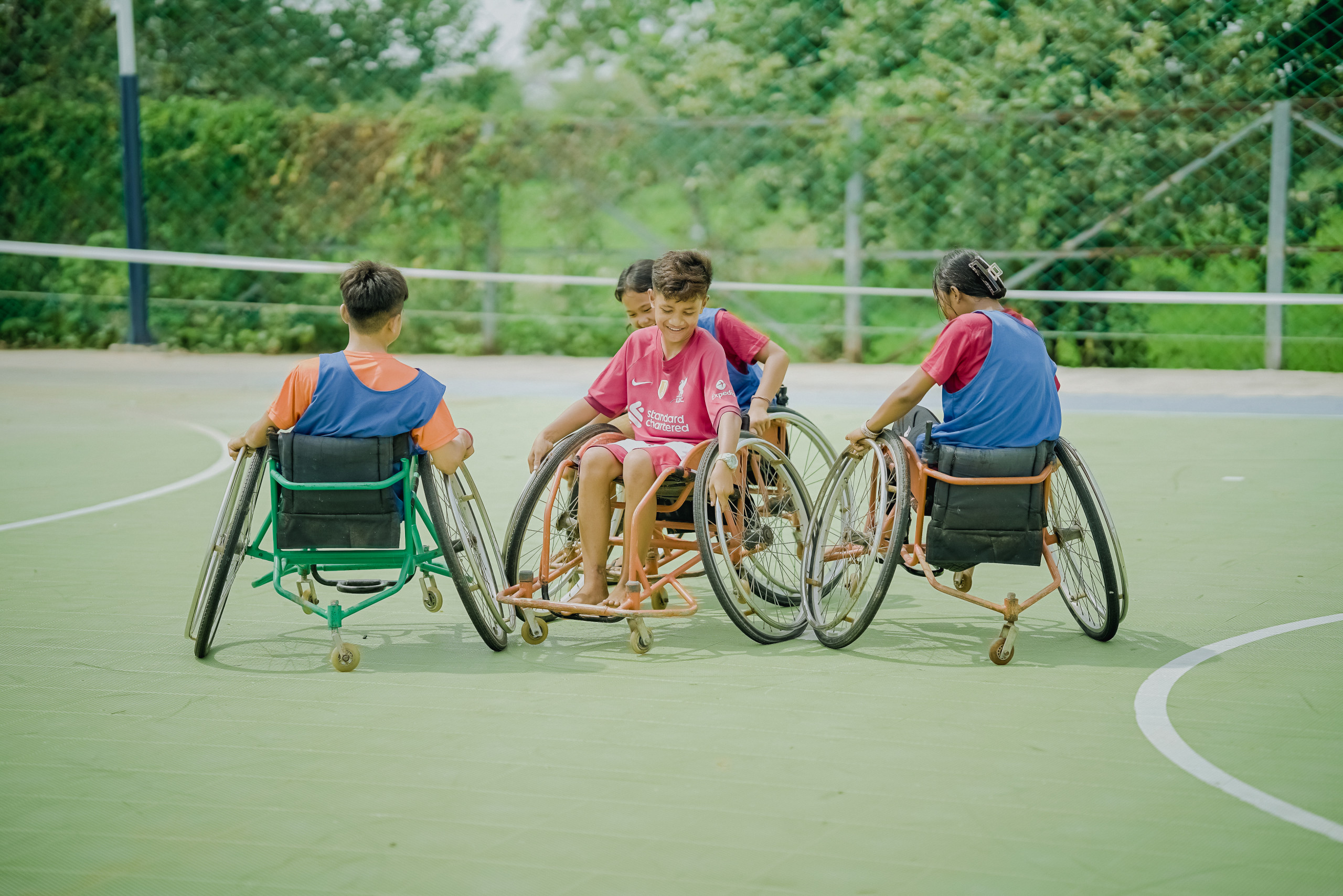 Children in wheelchairs play together on an outdoor sports court.