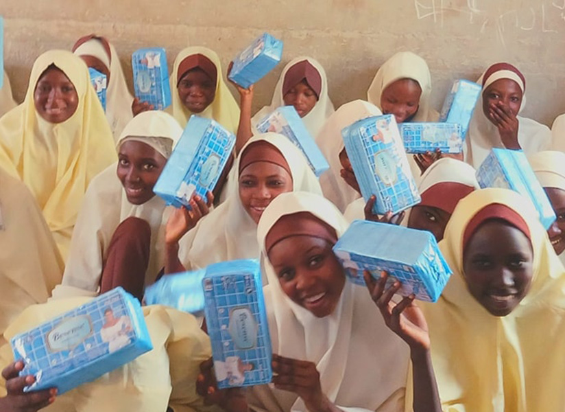Smiling girls in cream-colored headscarves hold up blue handbooks.