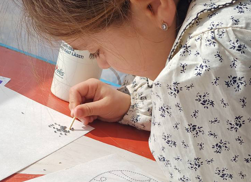 A young girl concentrates as she dots paint onto paper for a craft project.
