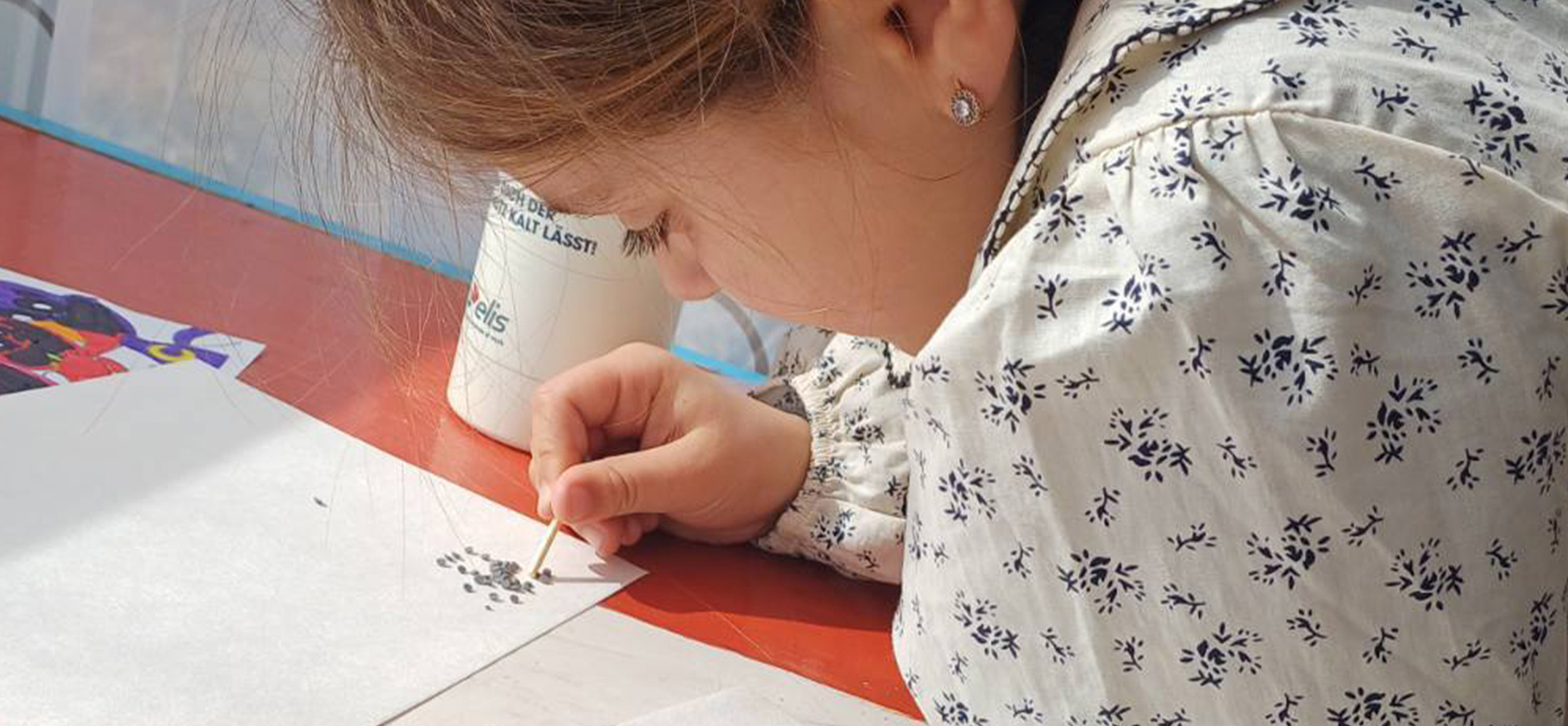 A young girl concentrates as she dots paint onto paper for a craft project.