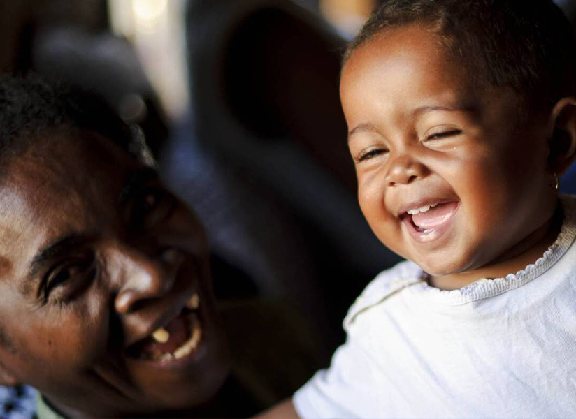 A laughing baby is held close by a smiling older woman.