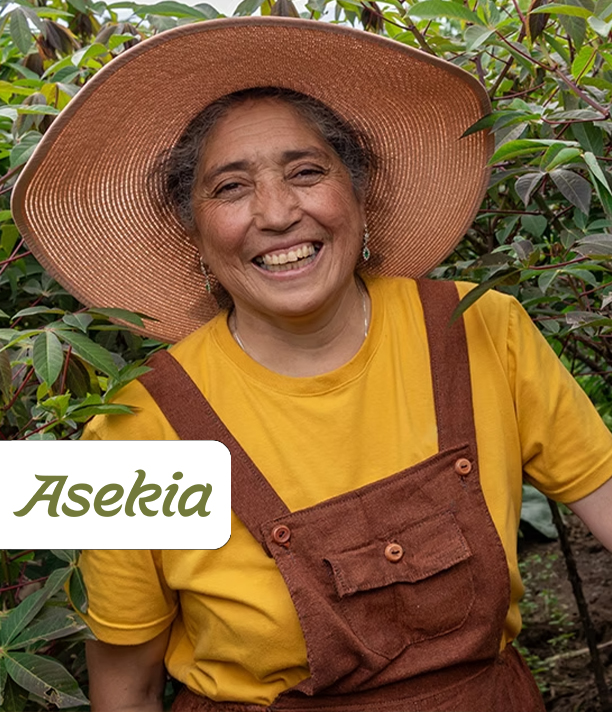 A smiling woman in a wide-brimmed hat and overalls stands among leafy crops, beside the Asekia logo.