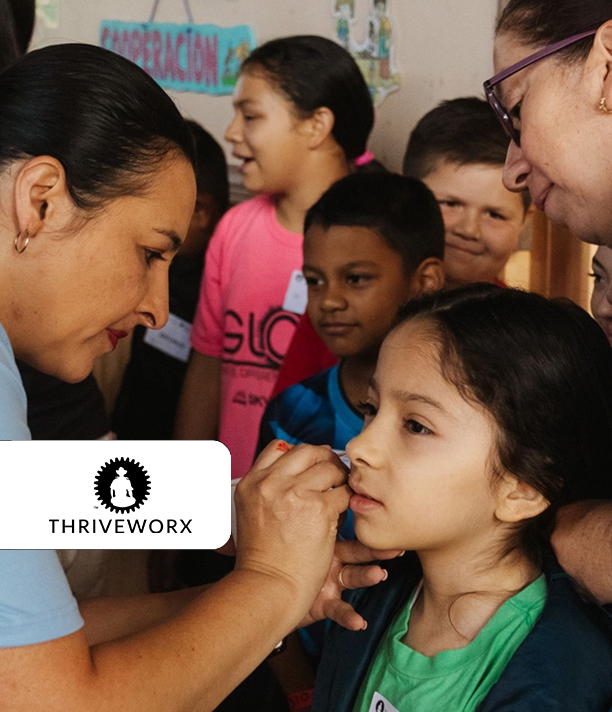 A volunteer paints a young girl's face as other children watch, beside the ThriveWorx logo.
