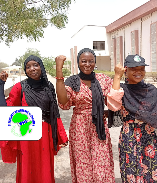 Three smiling young women raise their fists together outside a building, beside the Serendipity Healthcare Foundation logo.