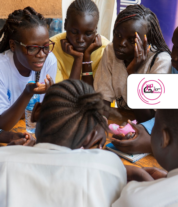 Girls gather closely around a table, listening as one explains something, beside the GoGirls ICT logo.