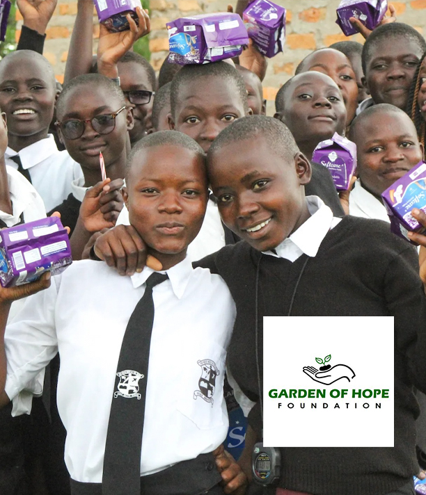 Smiling schoolgirls in uniforms hold up packages of sanitary pads, beside the Garden of Hope Foundation logo.